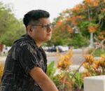 Relaxed man with glasses in a Yucatan park surrounded by vibrant flora.